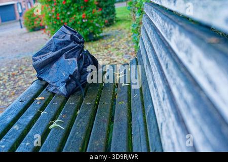 Un vieux banc en bois imbibé de pluie tient un parapluie pliant noir oublié, sa surface humide reflétant l'atmosphère humide et calme après un RA Banque D'Images