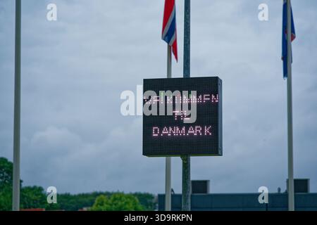 Un poteau métallique affiche un écran avec le message Velkommen til Danmark et Bienvenue au Danemark en danois et en anglais. Différents mâts de drapeau sont visibles dans Banque D'Images