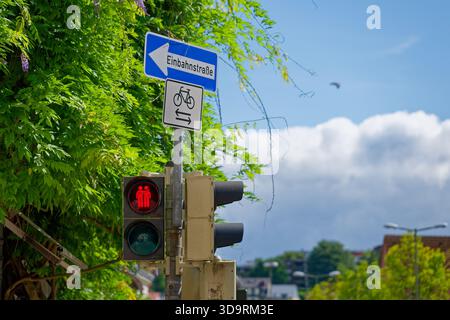 Un feu rouge montre deux personnes debout bras dans bras au-dessus d'un panneau indiquant Einbahnstrasse avec une flèche gauche et indiquant que les vélos peuvent circuler Banque D'Images