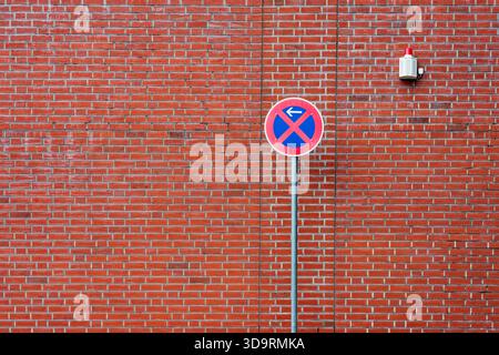 Un bâtiment en brique rouge montre un grand poteau avec un pas de stationnement et pas de panneau d'arrêt avec flèche à gauche. La vue de loin présente le contrôle du trafic urbain Banque D'Images