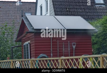 Un petit hangar en bois rouge avec des panneaux solaires sur le toit, entouré de verdure et une clôture en bois. Banque D'Images