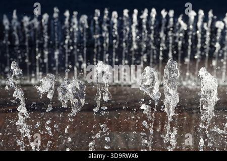 Une vue rapprochée des jets d'eau d'une fontaine, créant des éclaboussures et des gouttelettes dynamiques sur un arrière-plan flou. Banque D'Images