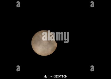 Une éclipse solaire partielle le 29 mars 2025, avec des nuages dans le ciel à midi, formant un croissant sur un fond sombre. Taches solaires et éruptions coronales a Banque D'Images