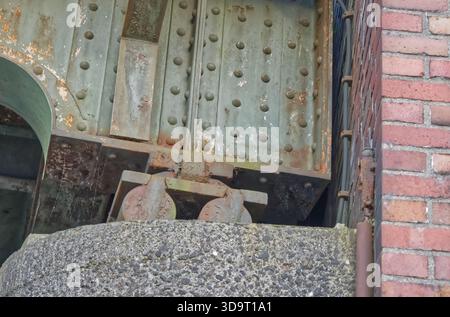 Vue rapprochée d'une structure métallique rouillée avec des roues, éventuellement une partie d'une ancienne machine industrielle ou d'un pont, contre un mur de briques. Banque D'Images