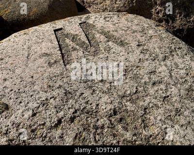 Vue rapprochée d'une grande roche altérée avec une lettre « M » sculptée sur sa surface. La roche est texturée et montre des signes d'âge, avec de la mousse et du lichen Banque D'Images