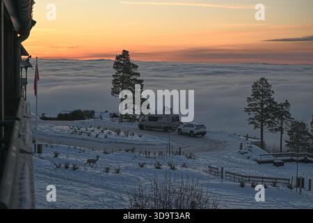 Un paysage hivernal serein avec une scène enneigée avec deux voitures garées sur une route sinueuse. En arrière-plan, une mer de nuages couvre la vallée en contrebas, Banque D'Images