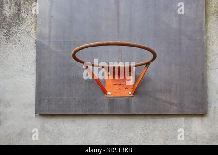 Vue rapprochée d'un panier de basket-ball contre un mur de béton texturé. Le cerceau est rouillé et orange, monté sur un panneau gris, mettant en vedette le spo urbain Banque D'Images