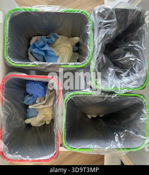 Quatre poubelles aux bords colorés, chacune contenant des gants usagés. Les bacs sont doublés de sacs en plastique transparents et sont disposés en grille. Banque D'Images
