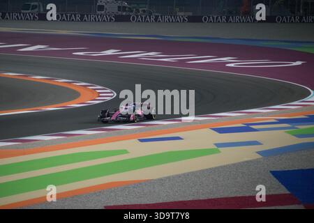 Les voitures concourent sur la piste au Grand Prix du Qatar de formule 1 2025 avec de l'asphalte coloré et des tribunes en arrière-plan pendant la course Banque D'Images