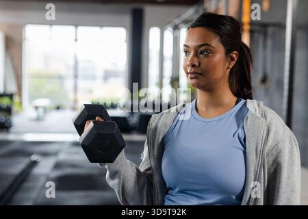Femme asiatique portant débardeur soulevant un haltère hexagonal au niveau des épaules dans l'espace de copie de gymnastique Banque D'Images