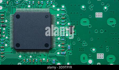 Gros plan d'une carte de circuit imprimé (PCB) verte avec une puce noire centrale et divers composants. Banque D'Images