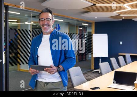 Homme dans les années 50 portant une chemise en denim tenant une tablette dans la salle de conférence près du tableau blanc, espace de copie Banque D'Images