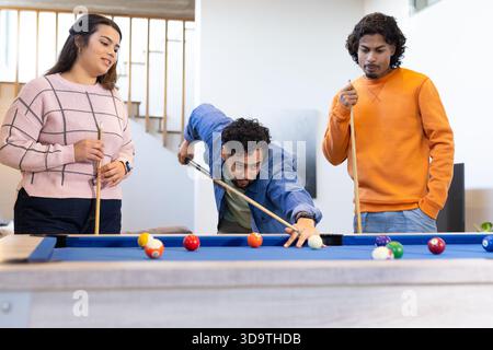 Amis jouant au billard avec des repères et des boules dispersées autour d'une table de billard en feutre bleu dans la salle de réception de la maison Banque D'Images