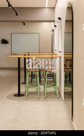 Groupe de trois tabourets vert pâle assis sous une table de bar en bois, miroir réfléchissant sol en terrazzo Banque D'Images