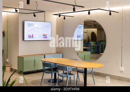 La table de réunion ovale en bois clair ancre la zone de collaboration avec des chaises bleues discrètes et un présentoir Banque D'Images