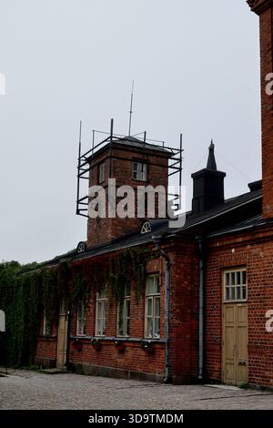 Bâtiment en briques rouges avec tour sur le toit et ossature en métal noir sous un ciel couvert par un matin brumeux à Suomenlinna Island, Helsinki, Finlande. Banque D'Images