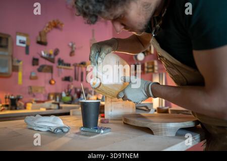 Homme menuisier se préparant au travail, mesurant la quantité requise de résine époxy sur une échelle à table. Banque D'Images