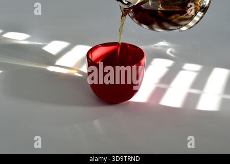 Une tasse de thé sur la table. Du thé est versé dans la tasse. Une ombre des stores sur la tasse. Banque D'Images
