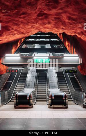 Stockholm, 15 mai 2024 : les escaliers mécaniques montent à travers une station de métro caverneuse ressemblant à un rocher rouge, guidant les navetteurs Banque D'Images