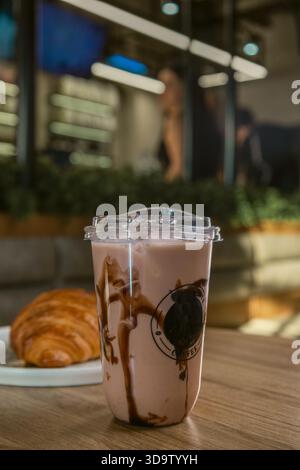 Boisson au chocolat glacé dans une tasse en plastique avec croissant sur la table Banque D'Images