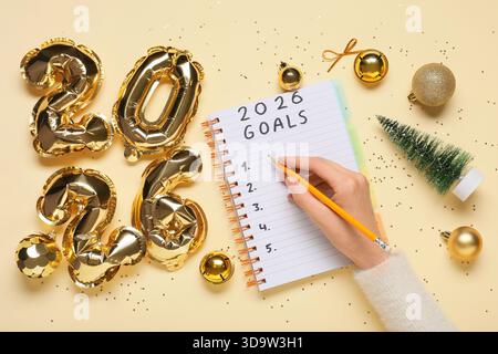 Femme avec la figure 2026 et décor de Noël écrivant la liste à faire sur fond jaune Banque D'Images