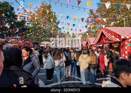 Marché en plein air surpeuplé avant le nouvel an avec des drapeaux colorés, des étals festifs et des gens marchant parmi des décorations de vacances lumineuses. Banque D'Images