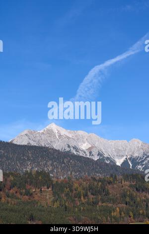 De majestueuses montagnes enneigées s'élèvent sous un ciel bleu vif, encadrées par des forêts luxuriantes. Banque D'Images