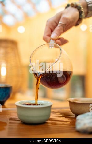 Un moment de verser du thé chaud dans un cadre traditionnel. Le flux concentré de thé fraîchement infusé relie la théière et la tasse, symbolisant le rituel Banque D'Images