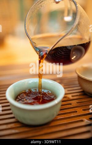 Un moment de verser du thé chaud dans un cadre traditionnel. Le flux concentré de thé fraîchement infusé relie la théière et la tasse, symbolisant le rituel Banque D'Images