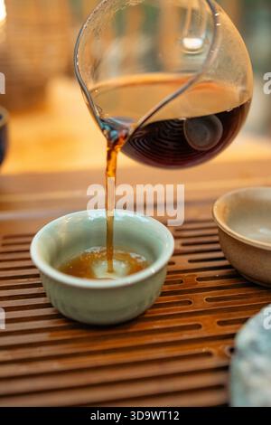 Un moment de verser du thé chaud dans un cadre traditionnel. Le flux concentré de thé fraîchement infusé relie la théière et la tasse, symbolisant le rituel Banque D'Images