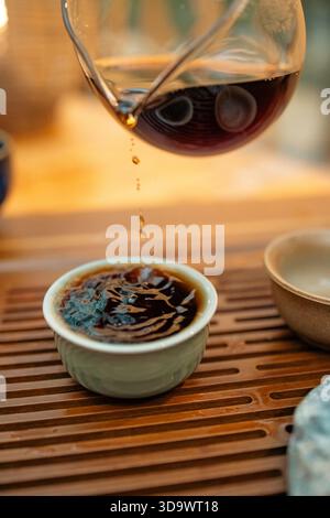 Un moment de verser du thé chaud dans un cadre traditionnel. Le flux concentré de thé fraîchement infusé relie la théière et la tasse, symbolisant le rituel Banque D'Images