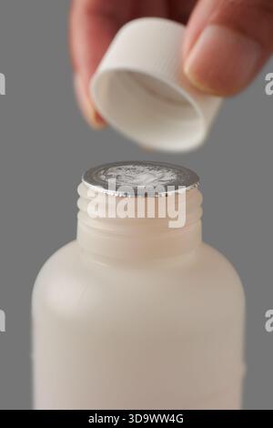 gros plan d'un flacon de médicament avec une fermeture de sécurité en aluminium intacte, un capuchon tenant la main au-dessus du récipient, un fond gris neutre isolé, un emballage inviolable Banque D'Images