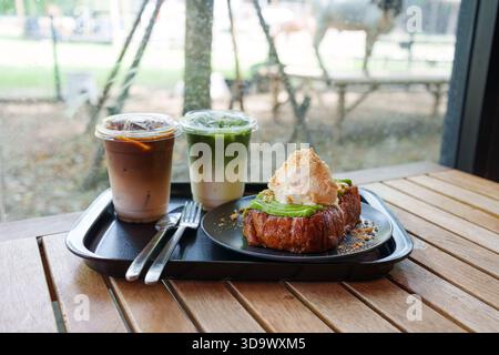 Ensemble de tranches de pain grillé garni de glace à la vanille, crème anglaise cuite à la vapeur avec café glacé, latte matcha glacé servi dans un plateau noir sur une table en bois Banque D'Images