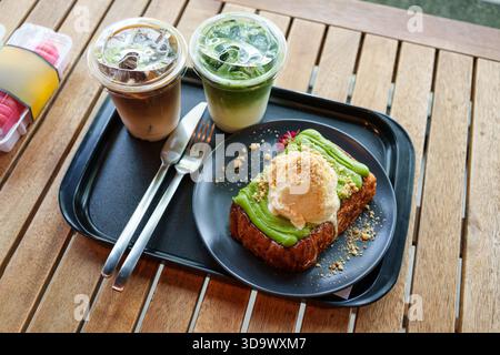 Ensemble de tranches de pain grillé garni de glace à la vanille, crème anglaise cuite à la vapeur avec café glacé, latte matcha glacé servi dans un plateau noir sur une table en bois Banque D'Images