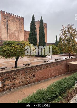 Vue pluvieuse sur les murs et jardins de la forteresse de l'Alhambra à Grenade, Espagne, avec des cyprès, des terrasses humides et une architecture mauresque. Banque D'Images