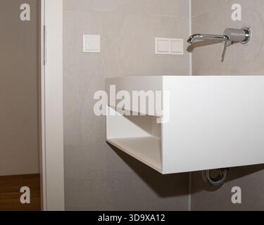 Salle de bains minimaliste avec meuble-lavabo blanc flottant, étagère à serviettes intégrée, carrelage neutre doux et robinet mural. Architecture propre Banque D'Images