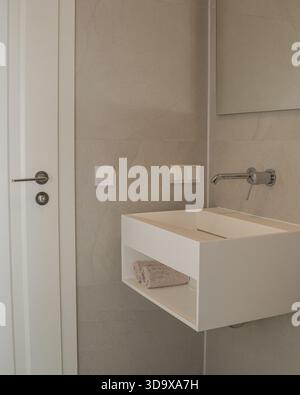 Intérieur de salle de bains minimaliste avec un lavabo blanc flottant, des carreaux de céramique neutres et des lignes contemporaines épurées. Éclairage doux et design fonctionnel Banque D'Images