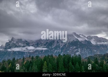 Montagnes alpines enneigées avec forêt et nuages bas par temps brumeux d'automne Banque D'Images