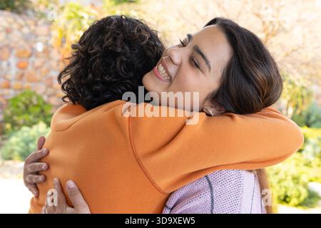 Amies féminines se serrant dans la cour du jardin ensoleillée portant un sweat-shirt et un pull en tricot Banque D'Images
