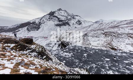Région de Skogafoss, Islande – 01 février 2022 : un randonneur se tient sur une pente rocheuse au-dessus de collines enneigées et d’une rivière partiellement gelée dans le paysage près de Skog Banque D'Images