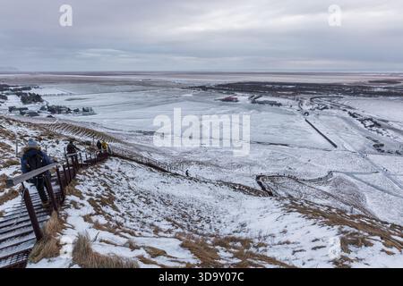 Région de Skogafoss, Islande – 01 février 2022 : un randonneur se tient sur une pente rocheuse au-dessus de collines enneigées et d’une rivière partiellement gelée dans le paysage près de Skog Banque D'Images