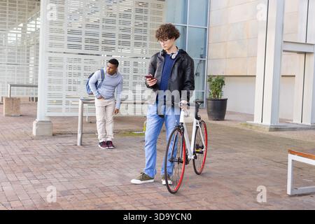 Divers amis s'appuyant contre la rampe dans la cour, ami vérifiant smartphone à côté du vélo, espace de copie Banque D'Images