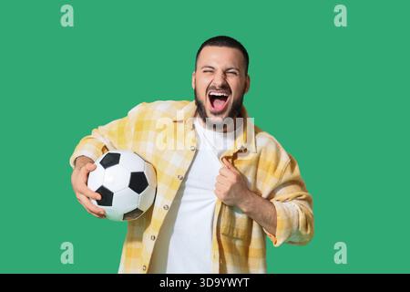 Fan de sport masculin avec ballon de football criant sur fond vert Banque D'Images