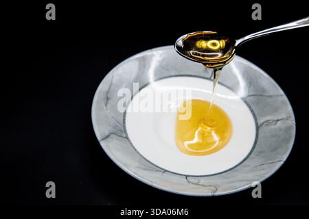 Gros plan de miel doré coulant d'une cuillère dans un bol sur un fond sombre, créant ainsi une photo riche et appétissante des détails culinaires. Banque D'Images