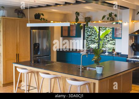 Îlot de cuisine en bois occupant le centre de dessin dans la cuisine avec des lumières suspendues et des tabourets de bar Banque D'Images
