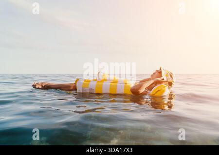 Femme, flotteur gonflable, Océan - détente sur un flotteur gonflable rayé jaune et blanc dans l'océan. Banque D'Images