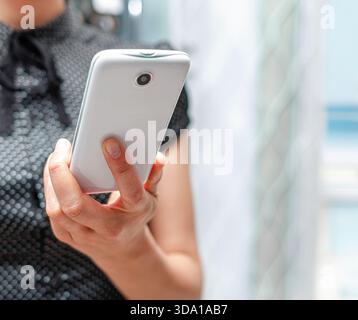 Une personne dans une chemise noire à motifs tient un smartphone blanc Banque D'Images
