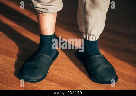 Vue à angle bas d'un homme détendu portant des chaussettes noires confortables sur des chaussettes sombres, debout sur des planches en bois chaudes avec des ombres spectaculaires de la lumière du soleil. Sele Banque D'Images