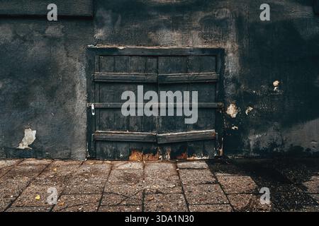 Gros plan Moody d'une ancienne porte en bois fortement altérée dans un mur de plâtre sombre en ruine. Texture cinématique parfaite pour le mystère, l'abandon, Banque D'Images