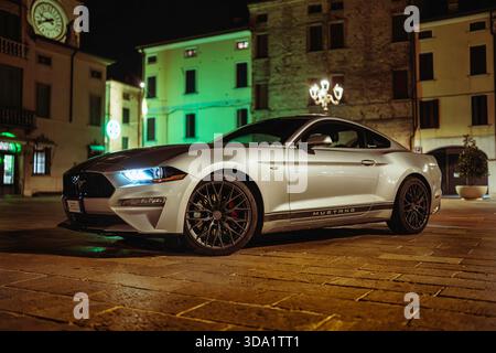 VO, italie 28 octobre 2025 : ford Mustang coupé garé sur des pavés sur une place illuminante de la vieille ville la nuit, mettant en valeur le style de vie urbain et le luxe Banque D'Images